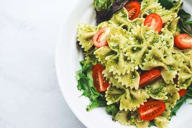 bowtie pasta on a plate with homemade pesto and sliced cherry tomatoes