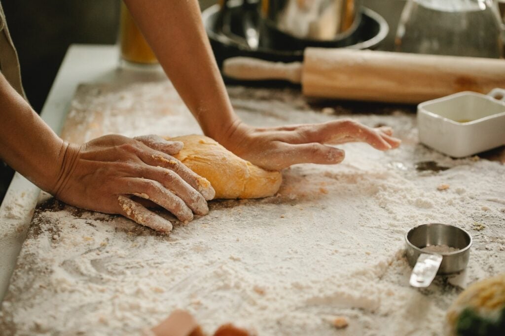 person making homemade bread by kneading dough on cutting board