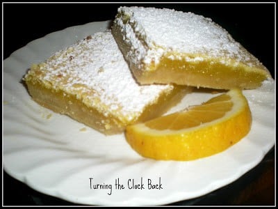 homemade lemon bars topped with confectioners sugar on a white plate with fresh lemon slice