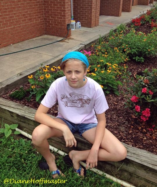 young girl sitting in front of butterfly garden with flowers and plants