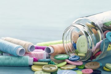 Multicolored buttons and spools of thread on light blue background - sewing concept