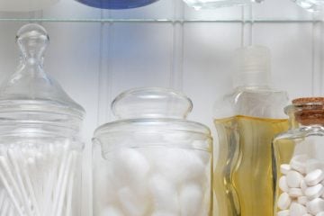 Closeup of two shelves of a medicine cabinet. A bottle of tablets, cotton balls and cotton swabs and assorted jars and bottles of soap and lotions. Square format.