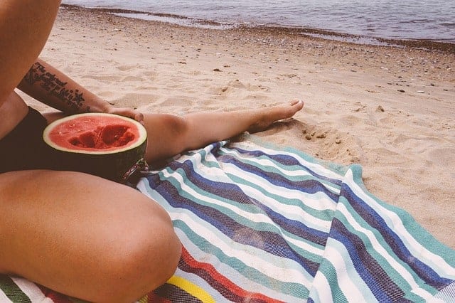 woman on beach eating watermelon on towel