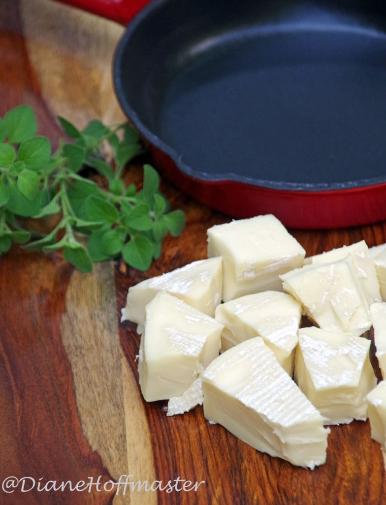 baked brie ingredients including brie and oregano near cast iron pan