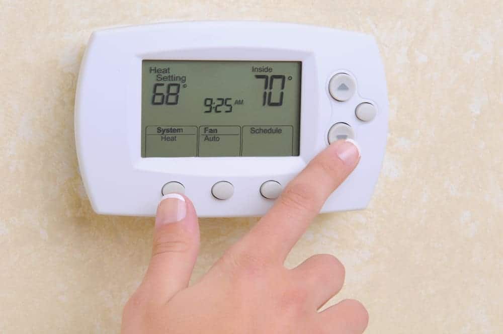 Closeup of a womans hand setting the room temperature on a modern programmable thermostat.