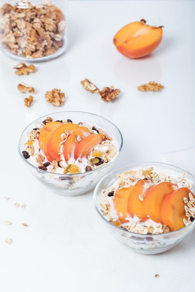 yogurt with fruit and walnuts in a bowl on a white surface