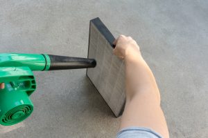 Woman hand holding blower to clean dirty air purifier HEPA filter.