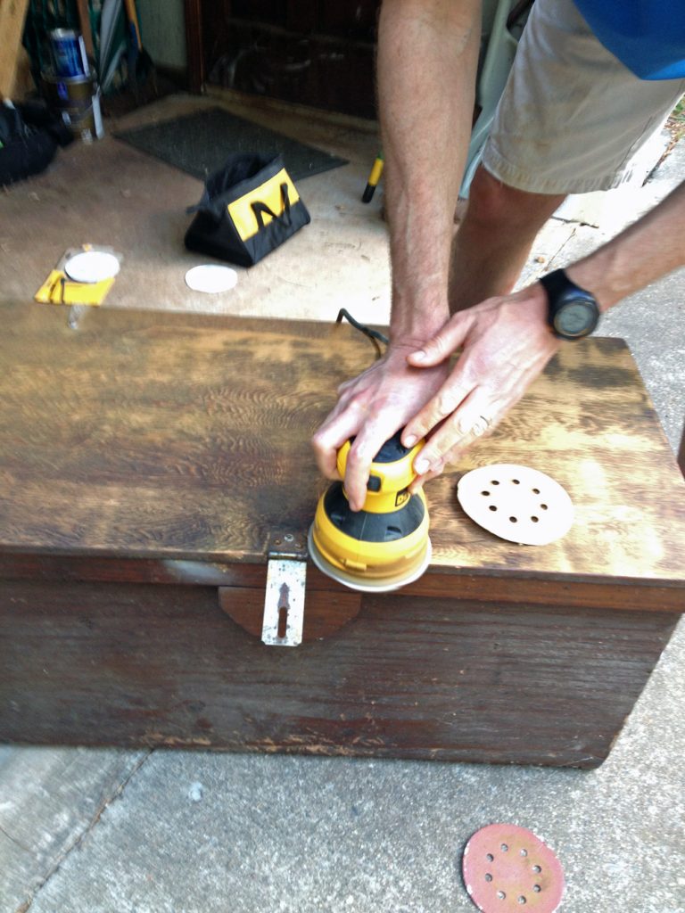 person sanding old linen chest in garage