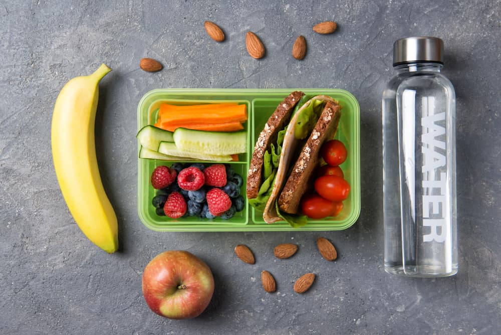 School lunch box with sandwich, vegetables, fruits and water on