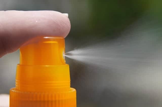 a person's finger on a spray bottle, spraying bee repellent 