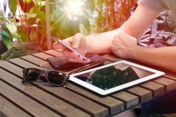 hands holding iphone with ipad on table outside