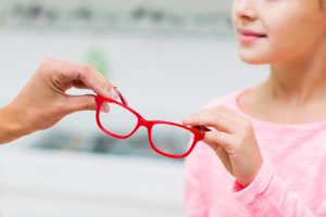 health care, people, eyesight and vision concept - close up of optician giving glasses to little girl at optics store