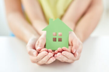 people, charity, family and home concept - close up of woman and girl holding green paper house cutout in cupped hands