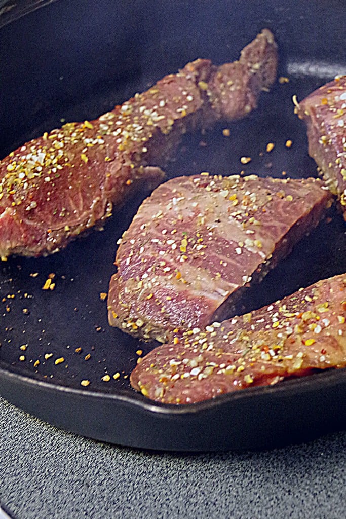 Steaks pan frying in cast iron with seasonings on them