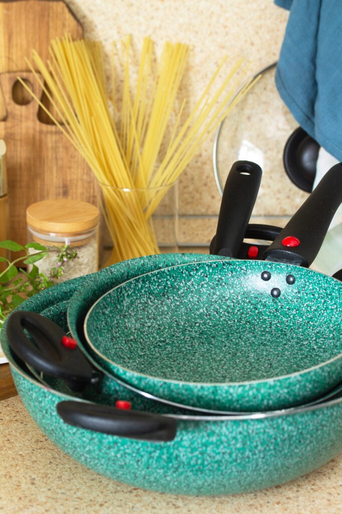 Set of empty ceramic coated dishes on a stone kitchen worktop surrounded. Kitchen table surrounded by Italian cuisine ingredients and frying pan.