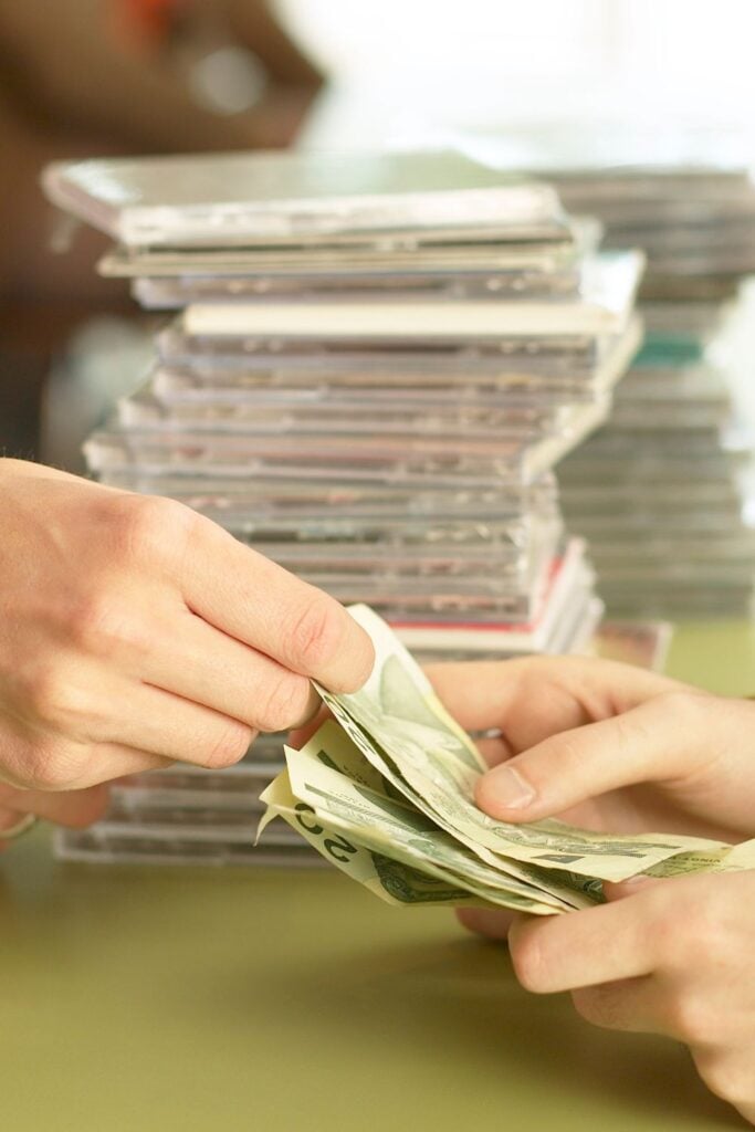 Pile of old cds with hands exchanging cash in front of them